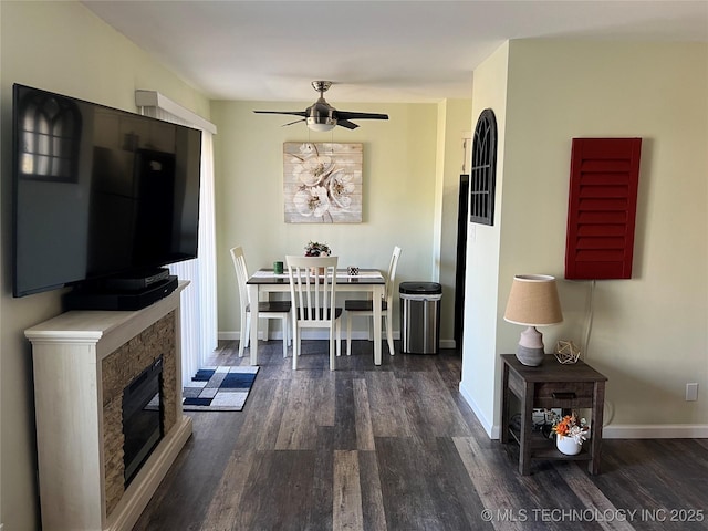 dining area with ceiling fan, a stone fireplace, and dark hardwood / wood-style flooring