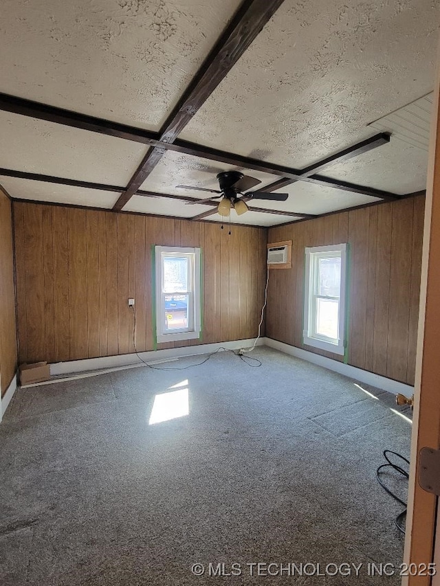 carpeted spare room with a wall mounted AC, a textured ceiling, wooden walls, ceiling fan, and beam ceiling