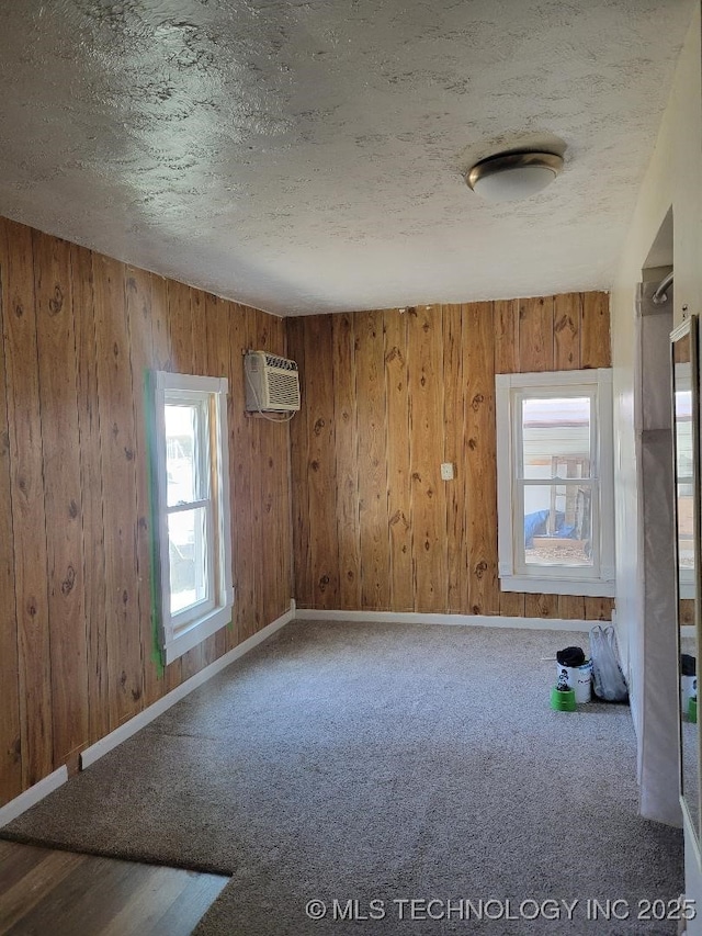 carpeted spare room featuring a wall mounted AC, a textured ceiling, and wood walls