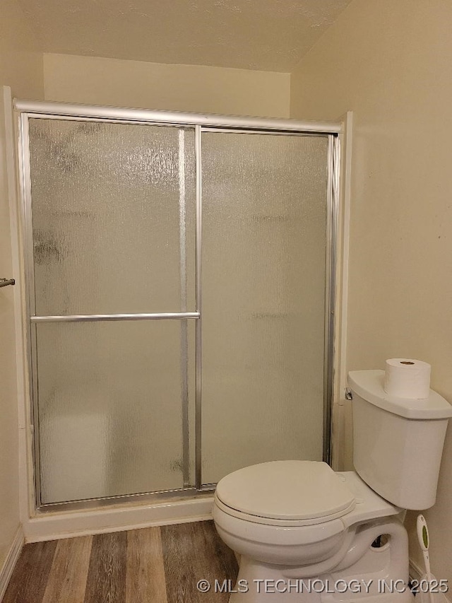 bathroom featuring hardwood / wood-style flooring, a shower with shower door, and toilet