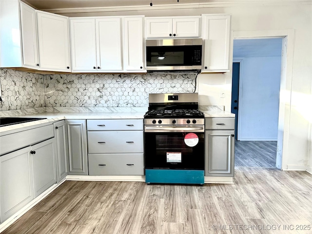 kitchen featuring tasteful backsplash, light wood-type flooring, white cabinets, and appliances with stainless steel finishes