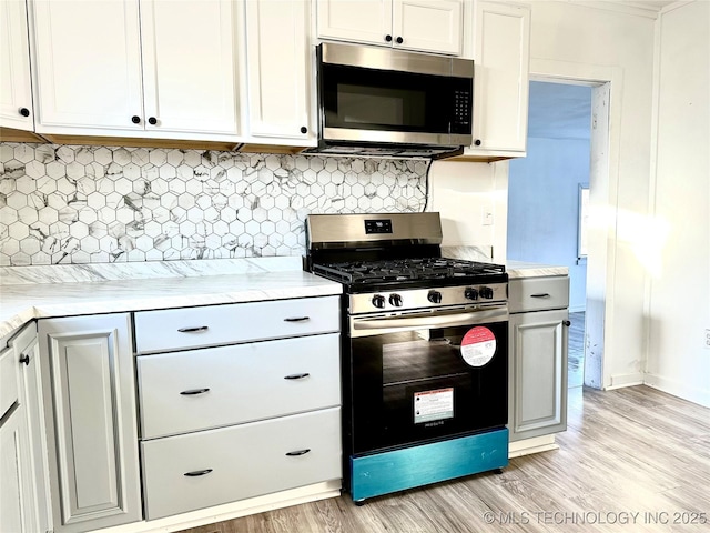 kitchen with backsplash, light hardwood / wood-style floors, white cabinets, and appliances with stainless steel finishes