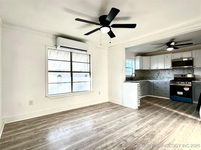 kitchen with sink, appliances with stainless steel finishes, backsplash, wood-type flooring, and an AC wall unit