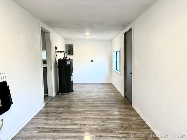 hallway with heating unit, electric water heater, and hardwood / wood-style floors