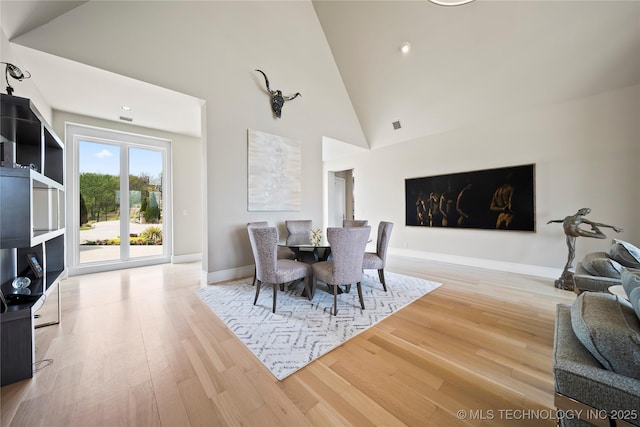 dining space featuring baseboards, high vaulted ceiling, and wood finished floors