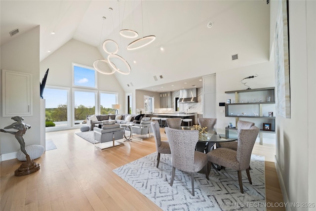 dining room with high vaulted ceiling, visible vents, light wood finished floors, and an inviting chandelier