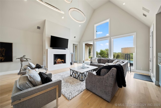 living area with light wood-style floors, a lit fireplace, visible vents, and high vaulted ceiling