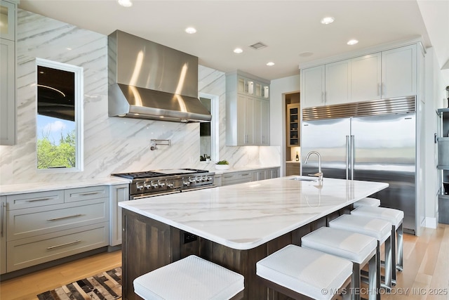 kitchen with range hood, a kitchen island with sink, glass insert cabinets, and premium appliances