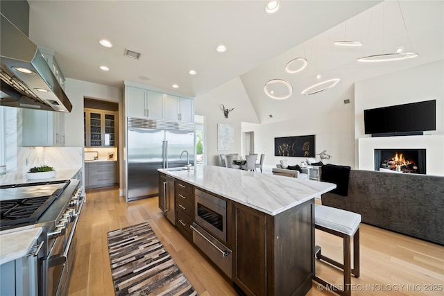 kitchen with a center island with sink, white cabinets, open floor plan, built in appliances, and extractor fan