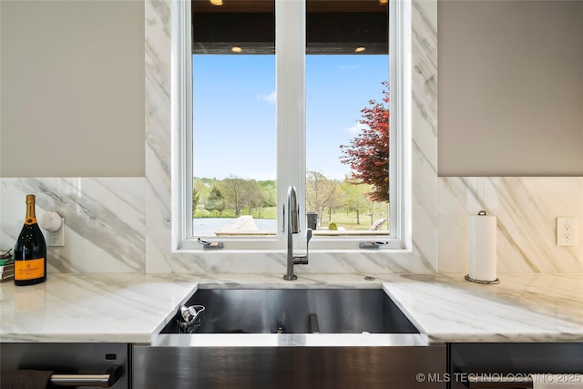 kitchen with light stone counters, a sink, and tasteful backsplash