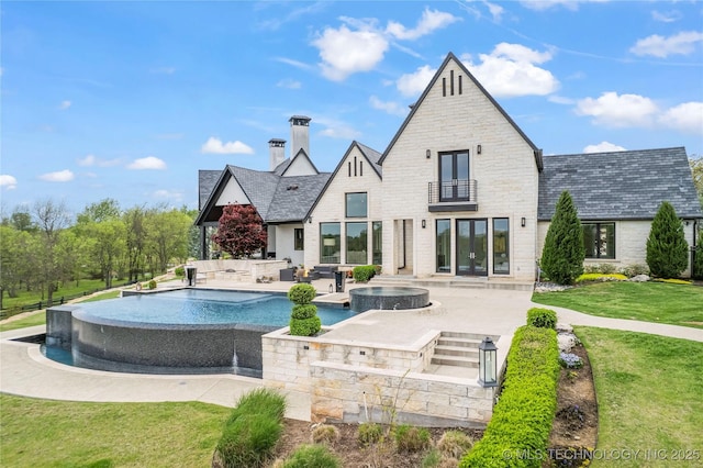 rear view of house with an in ground hot tub, a yard, a balcony, and a patio