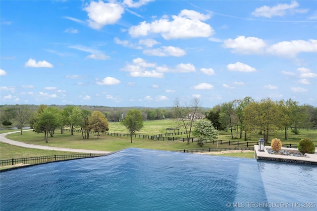 view of pool with a rural view, a water view, a lawn, and fence