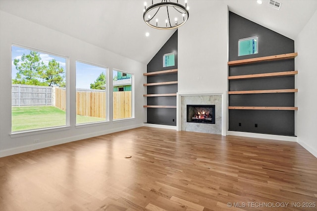 unfurnished living room featuring hardwood / wood-style flooring, built in features, a premium fireplace, an inviting chandelier, and high vaulted ceiling