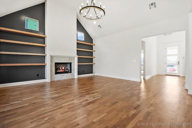 unfurnished living room featuring built in features, high vaulted ceiling, wood-type flooring, a notable chandelier, and a premium fireplace