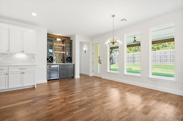 interior space with white cabinetry, wine cooler, decorative backsplash, hanging light fixtures, and dark wood-type flooring