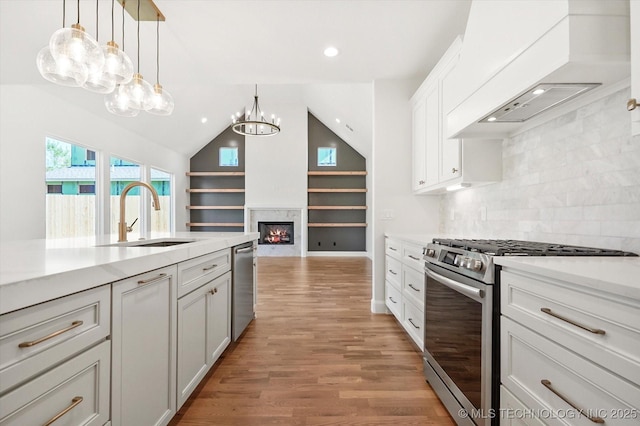 kitchen with sink, premium range hood, appliances with stainless steel finishes, decorative light fixtures, and light wood-type flooring