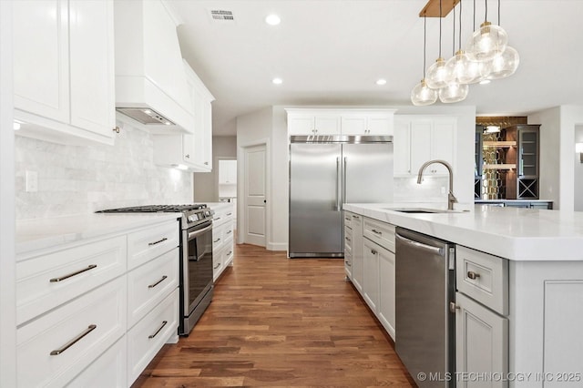 kitchen with sink, appliances with stainless steel finishes, an island with sink, white cabinets, and decorative light fixtures