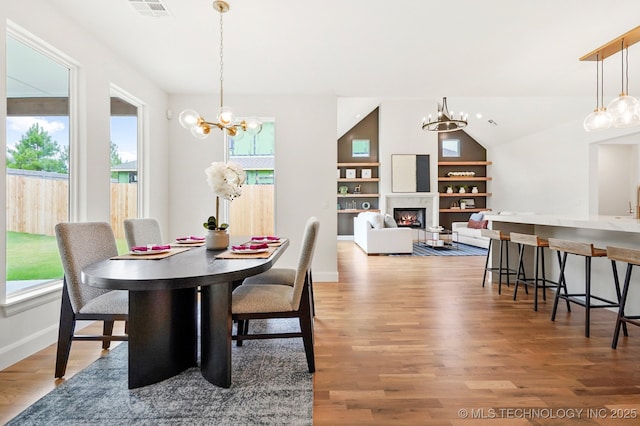 dining space with lofted ceiling, hardwood / wood-style flooring, built in features, and a chandelier