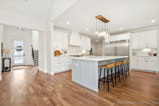 kitchen featuring premium range hood, pendant lighting, a center island with sink, and white cabinets