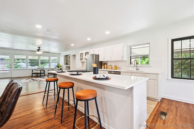 3006 E 21st St, Tulsa, OK 74114 - kitchen with appliances with stainless steel finishes, light wood finished floors, a breakfast bar area, white cabinets, and a center island