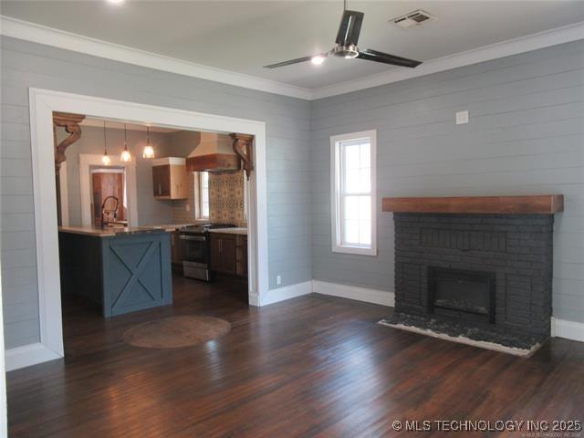 unfurnished living room featuring sink, crown molding, a brick fireplace, dark hardwood / wood-style floors, and ceiling fan