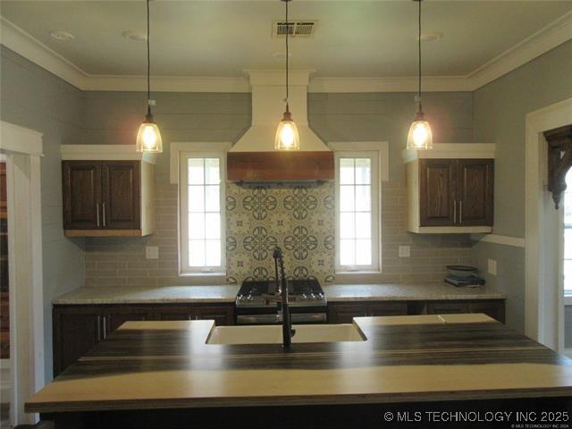 kitchen with a kitchen island with sink, sink, dark brown cabinets, and custom range hood