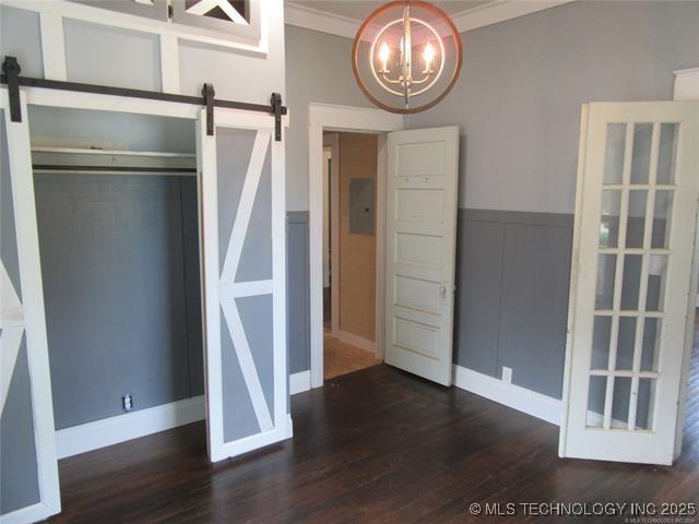 unfurnished bedroom with crown molding, a barn door, and dark wood-type flooring