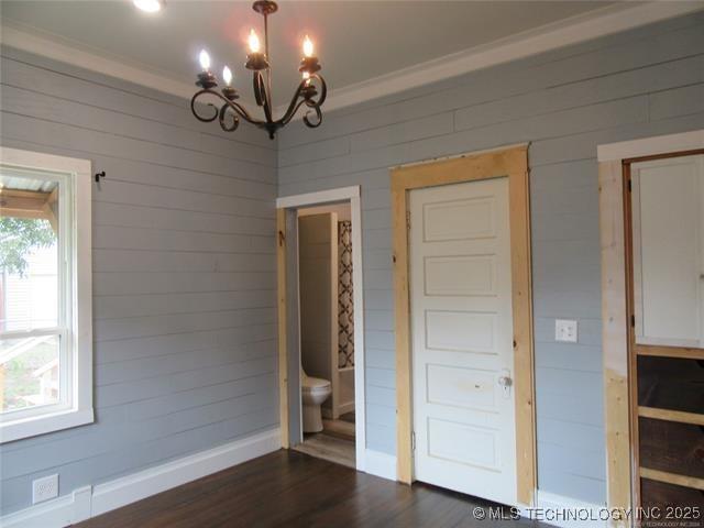 unfurnished bedroom with ensuite bathroom, dark hardwood / wood-style floors, a chandelier, and wood walls