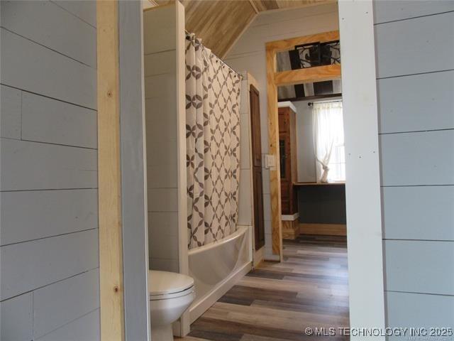 bathroom featuring wood-type flooring, wooden walls, toilet, and shower / bath combo with shower curtain