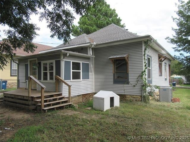 rear view of property with central AC unit and a lawn