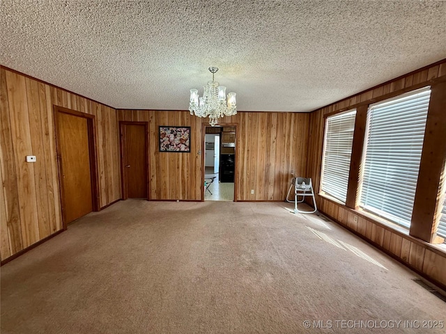 unfurnished room featuring carpet, a chandelier, and wood walls