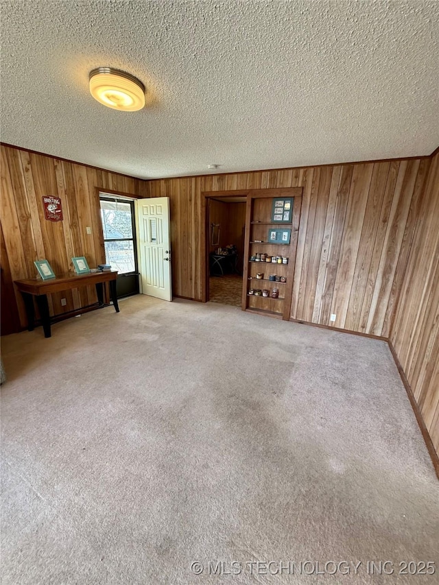 empty room featuring carpet, a textured ceiling, and wooden walls