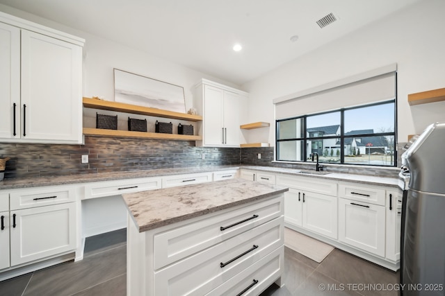 kitchen featuring light stone counters, stainless steel fridge, backsplash, sink, and white cabinetry