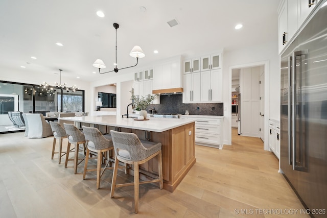 kitchen featuring appliances with stainless steel finishes, a notable chandelier, a large island with sink, white cabinets, and hanging light fixtures