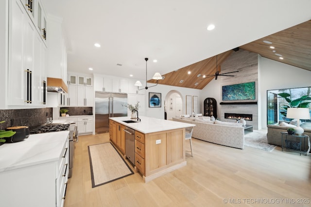 kitchen featuring decorative light fixtures, a large island with sink, light stone counters, white cabinets, and high quality appliances