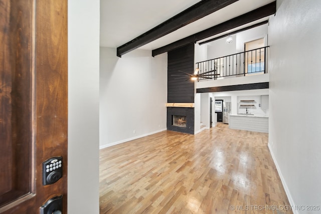 unfurnished living room with a high ceiling, beam ceiling, ceiling fan, and light hardwood / wood-style flooring