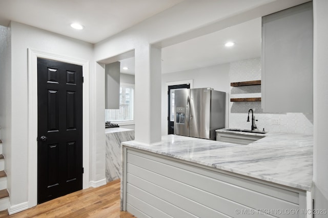 kitchen featuring light wood-type flooring, kitchen peninsula, stainless steel refrigerator with ice dispenser, light stone countertops, and sink