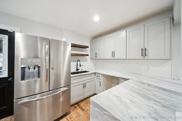 kitchen featuring light stone countertops, stainless steel fridge, light hardwood / wood-style floors, sink, and tasteful backsplash