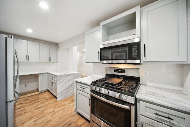 kitchen with appliances with stainless steel finishes, backsplash, light stone counters, light wood-type flooring, and white cabinetry