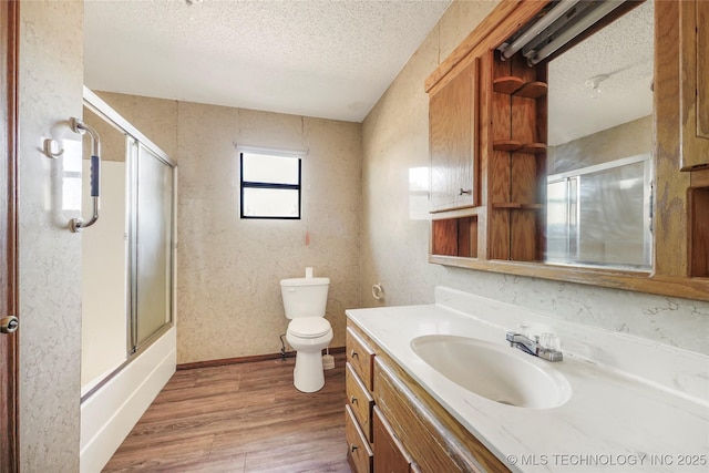 full bathroom with wood-type flooring, toilet, a textured ceiling, combined bath / shower with glass door, and vanity