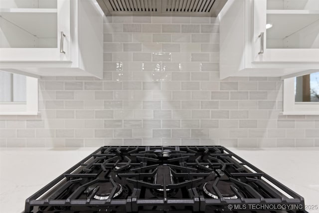 details featuring light stone countertops, black gas range, and backsplash