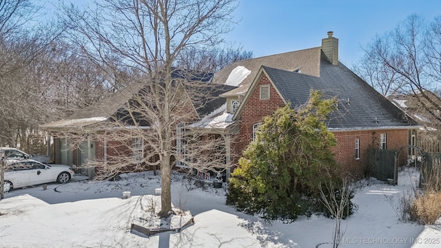 snow covered property with brick siding and a chimney