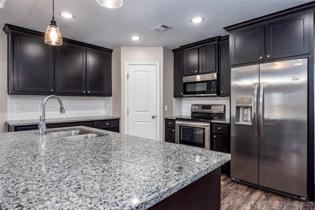 kitchen with appliances with stainless steel finishes, dark wood-type flooring, light stone counters, decorative light fixtures, and sink