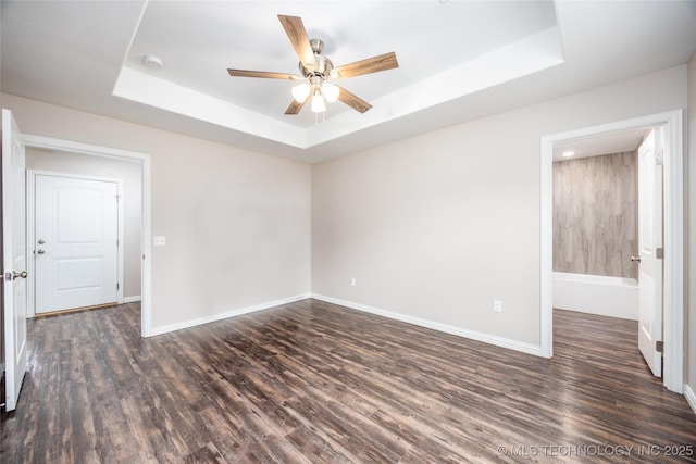 empty room with ceiling fan, a tray ceiling, and dark hardwood / wood-style floors