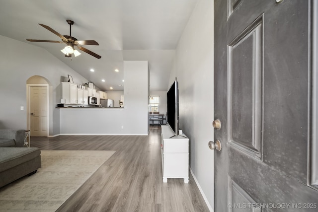 living area featuring arched walkways, ceiling fan, high vaulted ceiling, baseboards, and light wood-type flooring