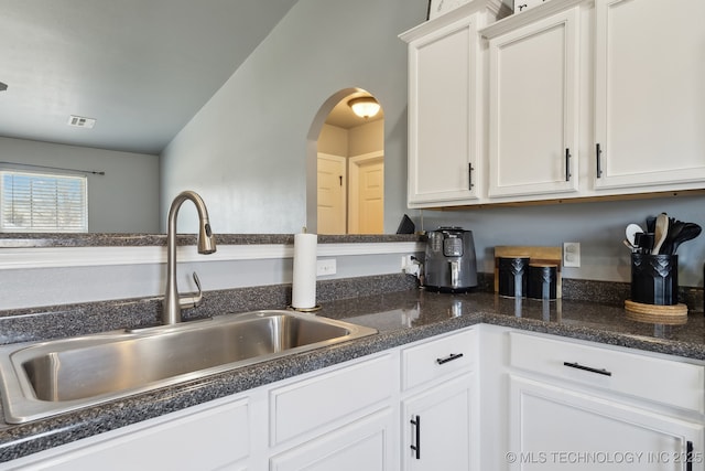 kitchen with visible vents, arched walkways, dark stone countertops, white cabinetry, and a sink