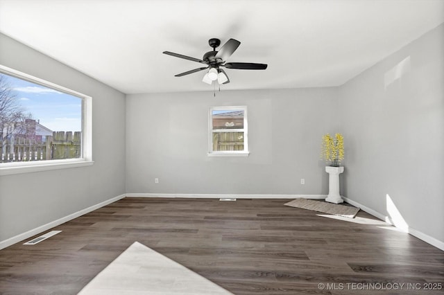 empty room featuring a ceiling fan, visible vents, baseboards, and wood finished floors