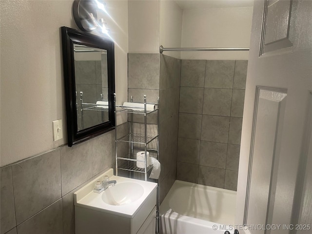 bathroom featuring tiled shower / bath, tile walls, and vanity