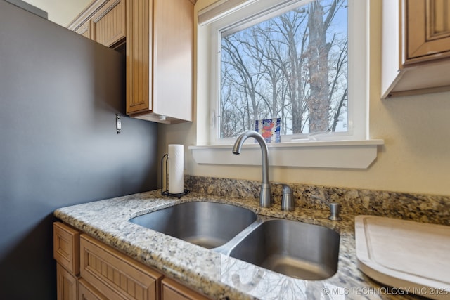kitchen with brown cabinets, a sink, and light stone countertops