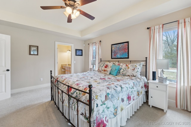 bedroom with a tray ceiling, light colored carpet, a ceiling fan, ensuite bath, and baseboards